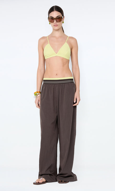 Woman wearing a yellow bikini top and brown wide-leg pants on a white background