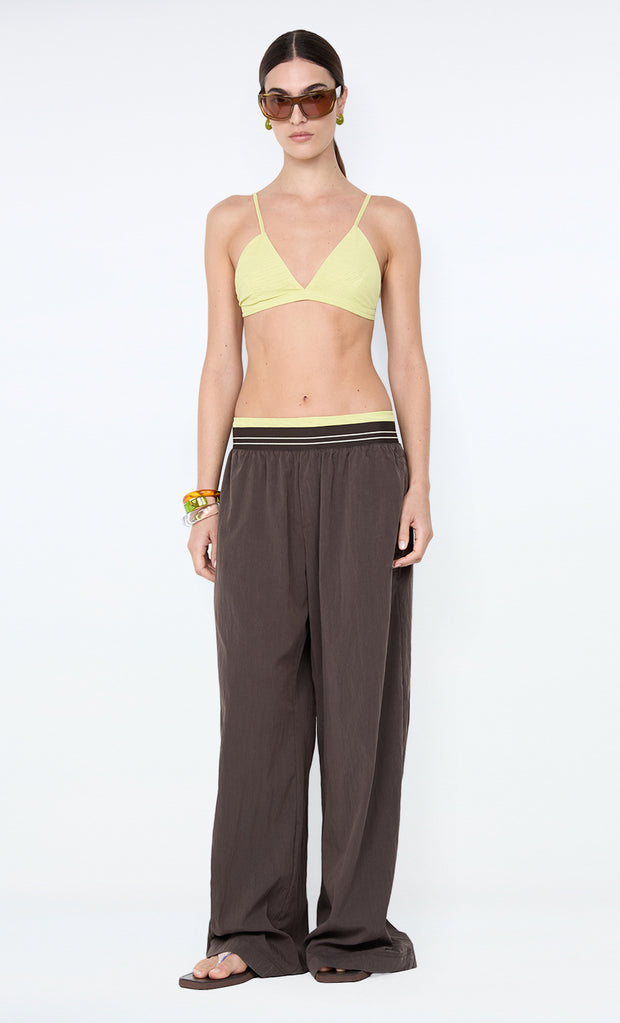 Woman wearing a yellow bikini top and brown wide-leg pants on a white background